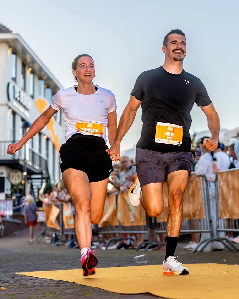 Twee lopers komen hand in hand en juichend over de finish van het Hardloopfeest