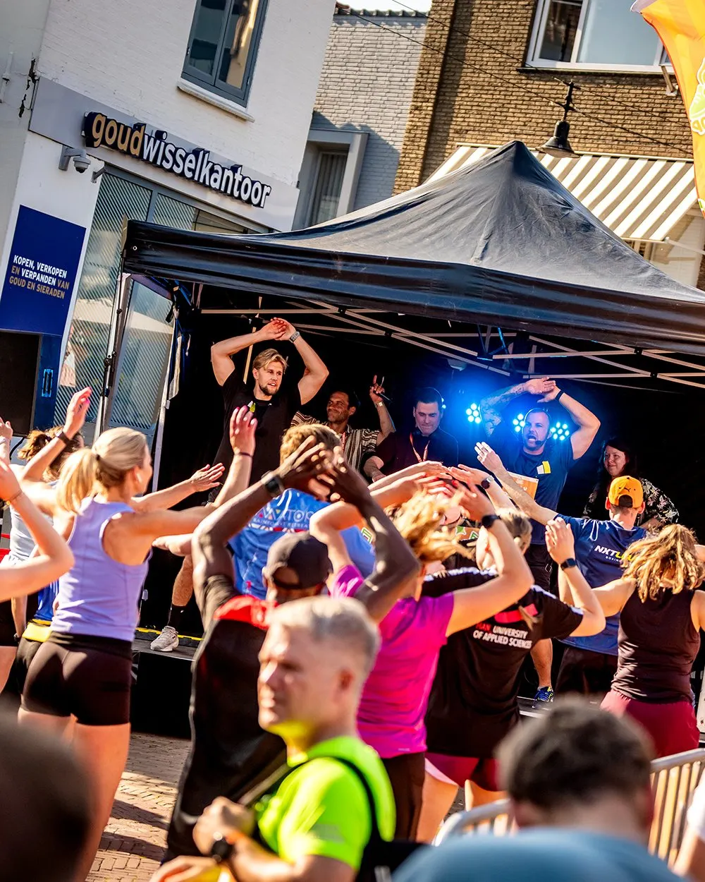 Lopers en publiek dansen met de handen in de lucht voor het muziekpodium van het Hardloopfeest